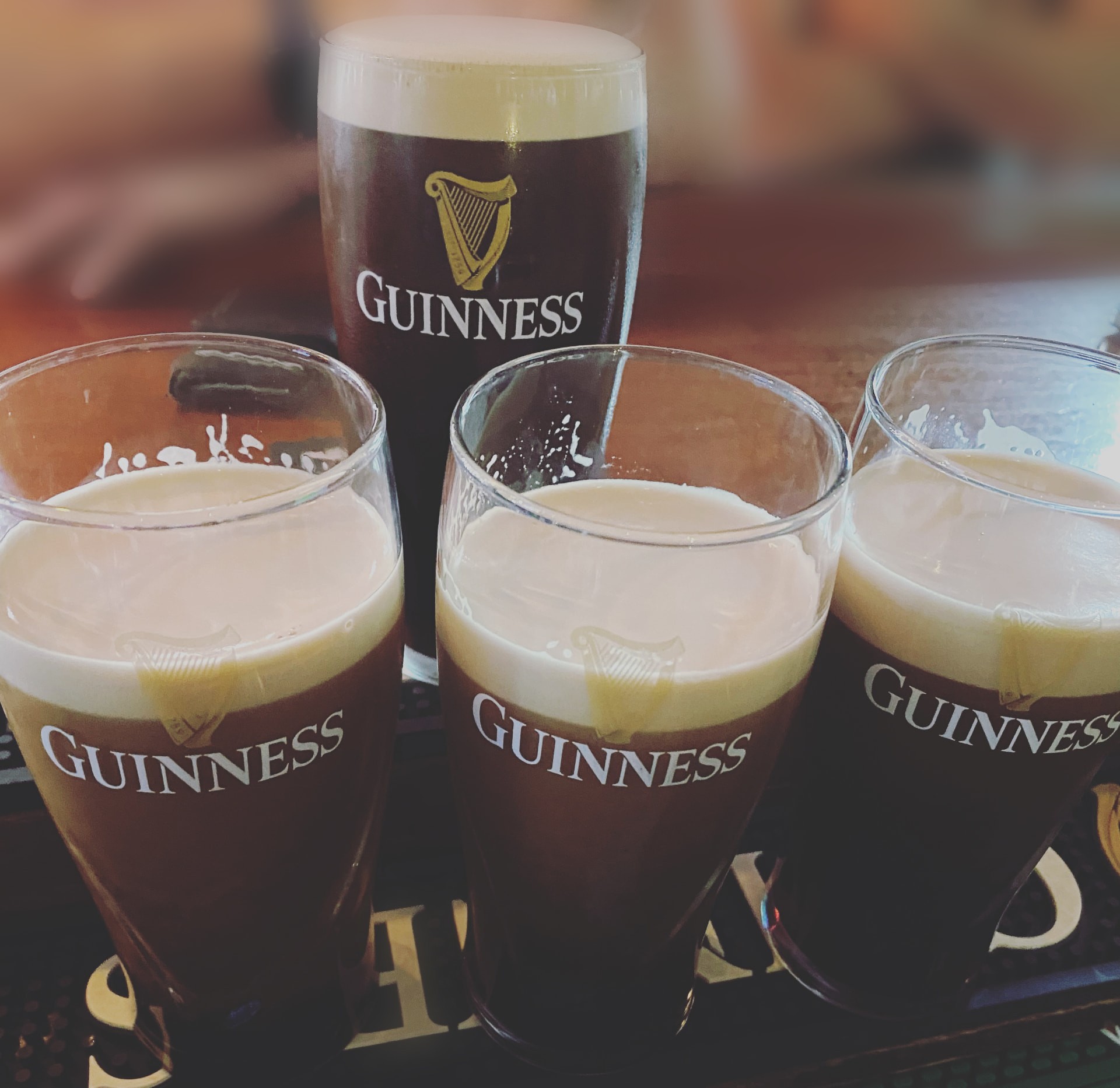Four freshly poured pints of Guinness in sharp focus on the bar at The Black Taxi, with the pub softly blurred behind them