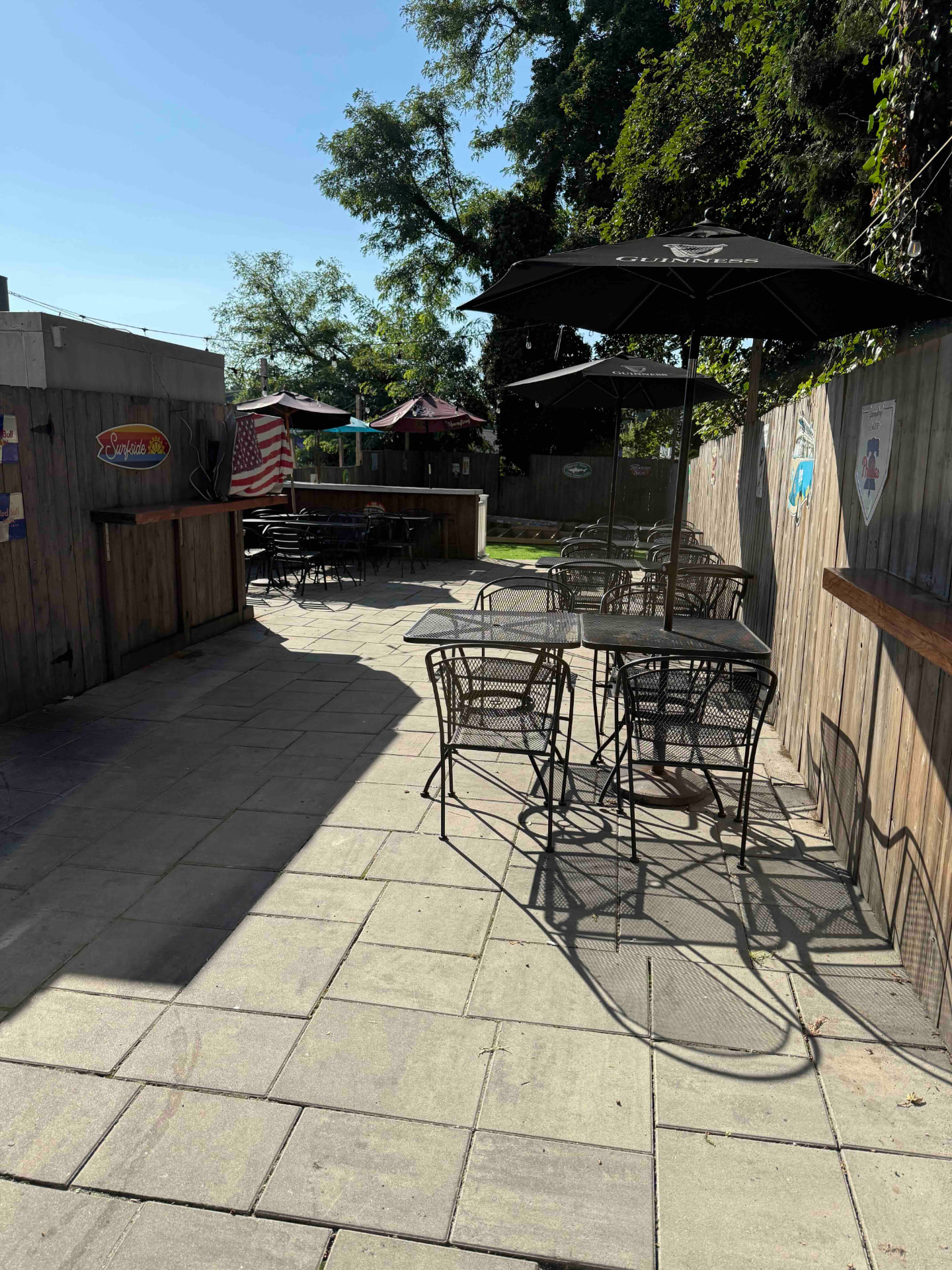 The Henry James outdoor patio with shaded tables, a wooden bar, and string lights on a sunny day